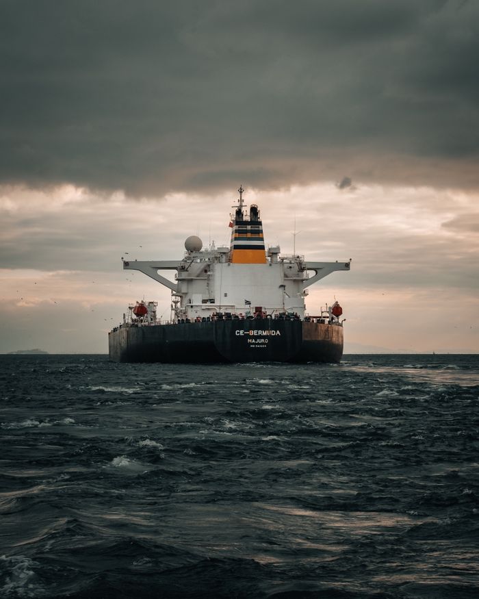 services-04 A large cargo ship navigating the open sea beneath a dramatic and cloudy sky, emphasizing industrial and maritime themes.