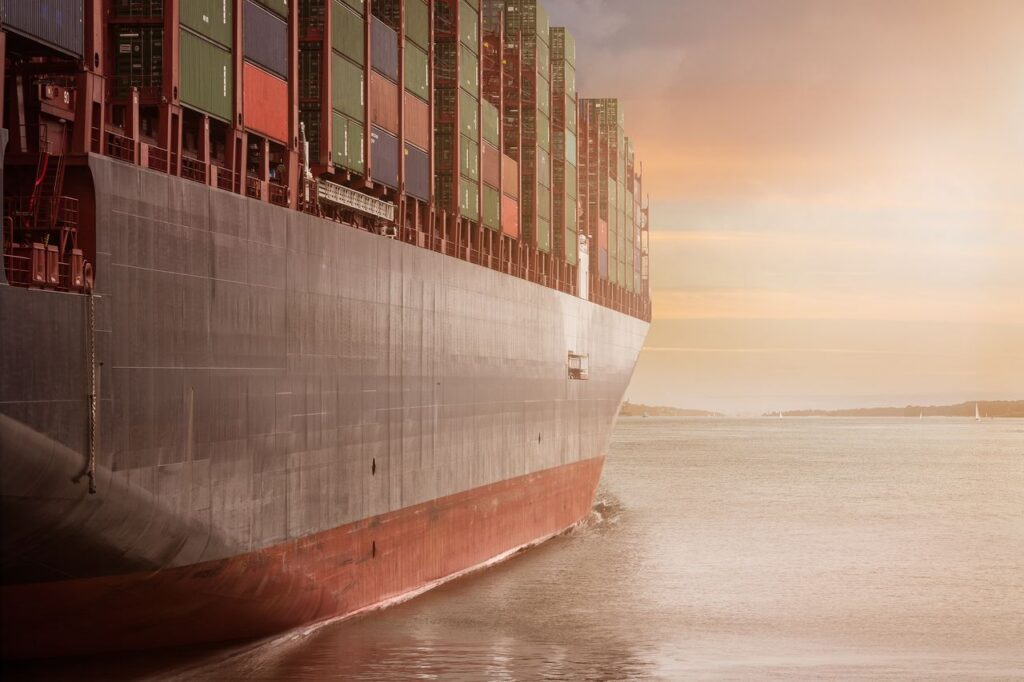 pexels photo 262353 A colossal cargo ship loaded with containers navigates through calm waters against a vibrant sunset sky.